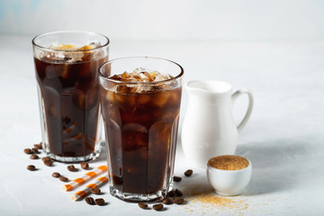 Ice coffee in a tall glass with cream poured over and coffee beans. Cold summer drink on a light blue background