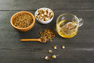 cup of chamomile tea with different size dried flowers on black wood table