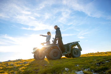 Beautiful couple is watching the sunset from the mountain sitting on atv quadbike © FS-Stock