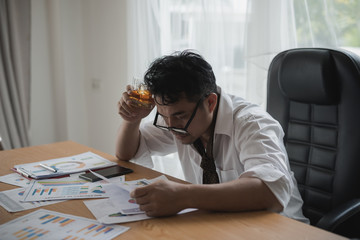 Businessman holding a glass of whiskey. he feel stressed, disappoint during working looking Data Charts,business document at office desk. alcohol addiction - drunk businessman concept