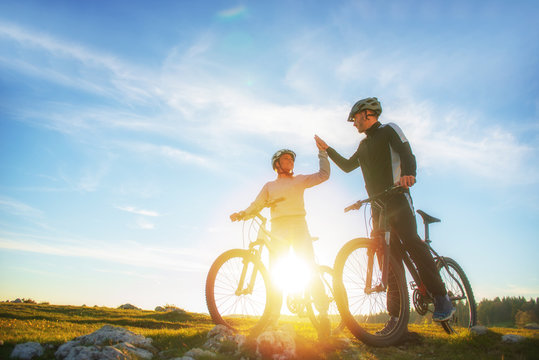 happy couple goes on a mountain road in the woods on bikes with helmets giving each other a high five