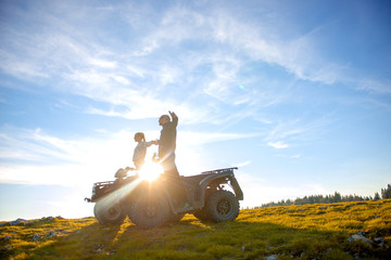 Beautiful couple is watching the sunset from the mountain sitting on atv quadbike © FS-Stock