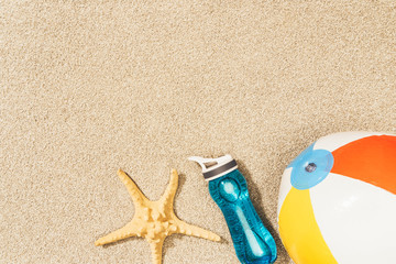 Fototapeta na wymiar flat lay with arranged water bottle, sea star and beach ball on sand