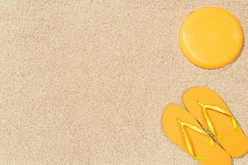 Fototapeta na wymiar top view of yellow flip flops and frisbee on sand