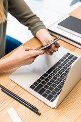 cropped shot of businesswoman using smartphone at workplace with laptop
