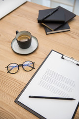close up view of cup of coffee, eyeglasses, documents on wooden tabletop