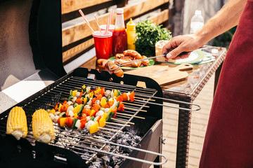 Man checking vegetables and sausages grilled for outdoors barbecue