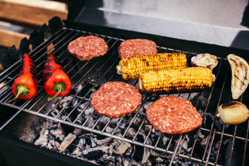 Meat patties and vegetables cooked outdoors on grill