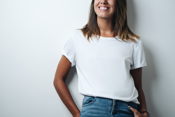 Obraz premium Smiling woman in white blank t-shirt, empty wall, horizontal studio close-up