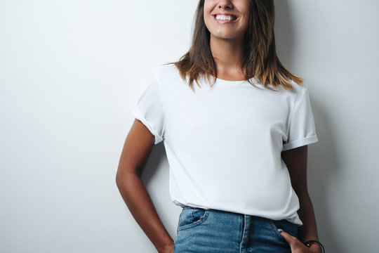 Smiling woman in white blank t-shirt, empty wall, horizontal studio close-up
