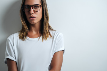 Beautiful woman in white blank t-shirt wearing glasses, empty wall, horizontal studio portrait