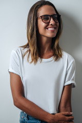 Pretty woman in white blank t-shirt wearing glasses, empty wall, verticalstudio portrait