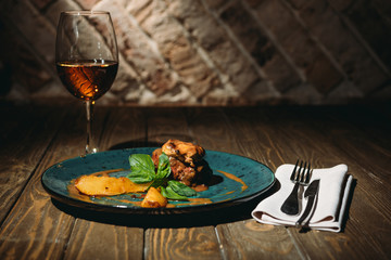 close up view of italian dish with basil leaves, glass of wine and cutlery on wooden surface