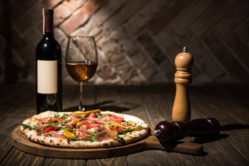 selective focus of italian pizza, spices in grinders, bottle and glass of wine on wooden tabletop