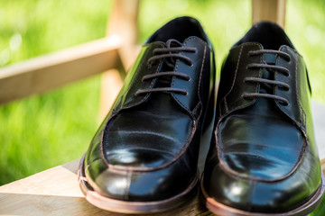 selective focus of black leather shoes on wooden stairs with green blurred background