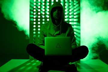 toned picture of hacker in hoodie with laptop and triangle sign on it