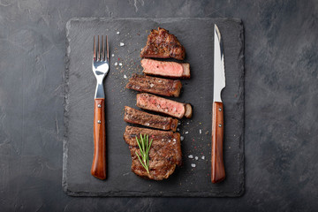 Closeup ready to eat steak new York beef breeds of black Angus with herbs, garlic and butter on a stone Board. The finished dish for dinner on a dark stone background. Top view