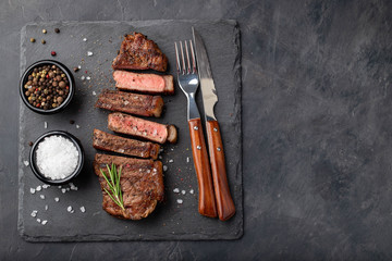 Closeup ready to eat steak new York beef breeds of black Angus with herbs, garlic and butter on a stone Board. The finished dish for dinner on a dark stone background. Top view with copy space