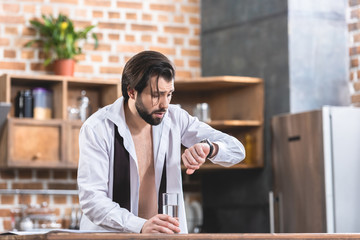 handsome loner businessman with hangover checking time at kitchen