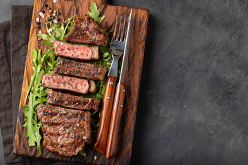 Closeup ready to eat steak new York beef breeds of black Angus with herbs, garlic and butter on a wooden Board. The finished dish for dinner on a dark stone background. Top view with copy space