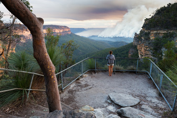 Woman at a bushwalking lookout with a view over a remote bushfire and smoke in the Blue Mountains,...