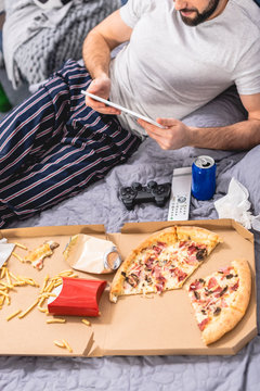 cropped image of loner using tablet with pizza on bed in bedroom