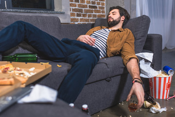  loner sleeping on sofa with glass of whiskey in dirty living room