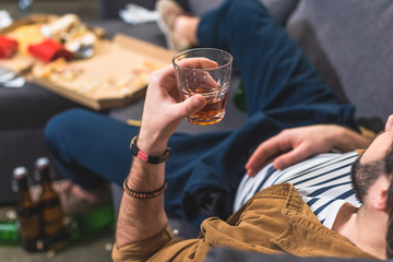 cropped image loner lying on sofa with glass of whiskey at living room