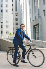handsome young businessman in stylish suit on bicycle in business district
