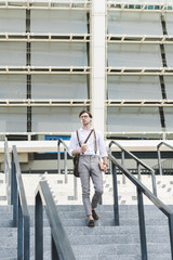 stylish young man walking down stairs in front of stadium with book and coffee to go