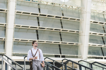 handsome young man standing on stairs in front of stadium with book and coffee to go