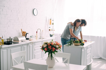 front view of young african american woman embracing boyfriend while he cooking at kitchen