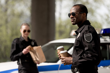 young police officers with coffee to go and paper bag with lunch having break