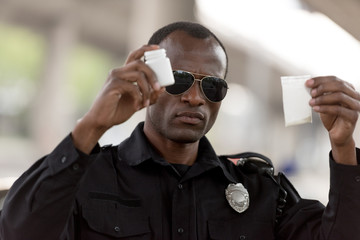 african american policeman holding drugs in plastic zipper and pills jar