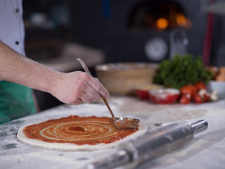 Fototapeta premium Chef smearing pizza dough with ketchup