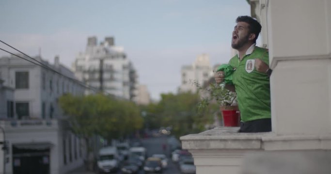 Happy Mexican football supporter waving jersey while celebrating victory in balcony