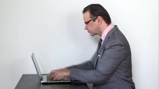 The man in the suit sitting at the desk and writing fast on the computer. Concentrated businessman writes speedy on laptop.