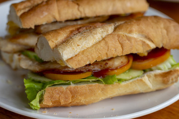Sandwich with salad and tomatoes on white plate closeup photo. French baguette with salad on wooden table.