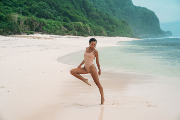 Fototapeta na wymiar Gorgeous woman runs along the beach with white sand. Female athlete is engaged in sports in the morning near the ocean on the island. Model in a swimsuit is jumping.