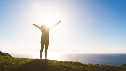 Excited woman stand on mountain hill with hands raised looking towards the ocean. Global female empowerment. Travel highlight in nature.