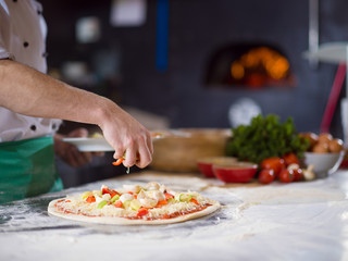 Obraz na płótnie Canvas chef putting fresh vegetables on pizza dough