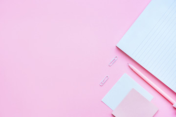 Beautiful office stationery flatlay with ruled notebook, pink pen, sticky note and paper clip on the bright desk with pink background.