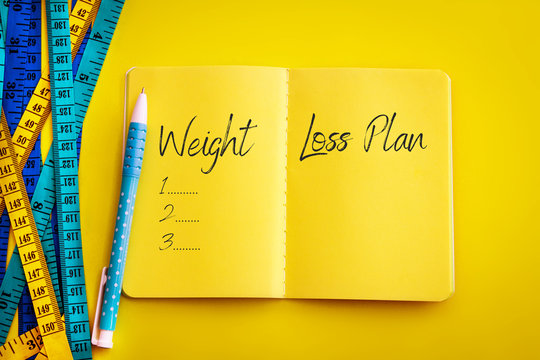 Weight loss and Diet control concept background. Colorful of Measuring tape on vibrant yellow color  background with blue book diary notepad and text as " Weight Loss Plan "  for a healthy fitness .