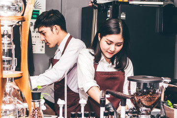 Portrait of couple barista working with coffee machine for making coffee and standing behind the counter bar in a cafe
