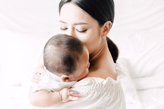 Mother holding baby in her arms and kiss in a white bedroom.Love of family concept