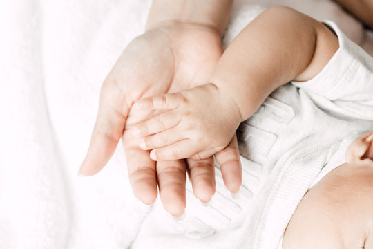 Mother holding sleeping baby hand on white bed.Love of family concept