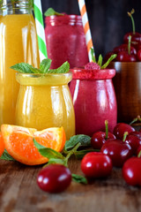 Yellow and red smoothies in glass jars surrounded by mandarins and cherries
