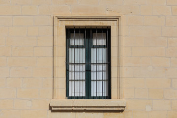 Fototapeta na wymiar Malta, Valletta. Facade of yellow limestone house with closed window with metal bars, that provides safety. Close up view.