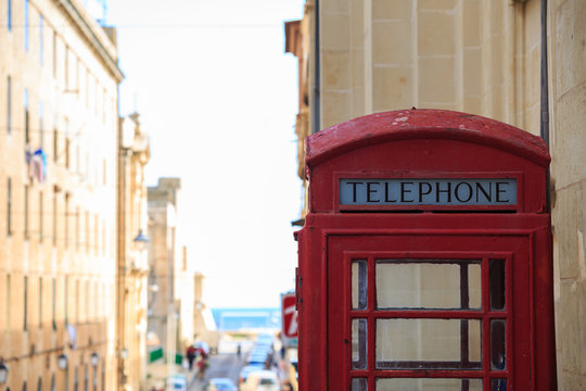 Red British telephone booth. Empty, vintage, peeled phone box in Valletta, Malta. Copyspace, close up view, blurred town background.