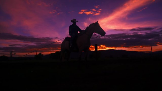a cowboy on a horse silhouetted against sky as the sun sets.